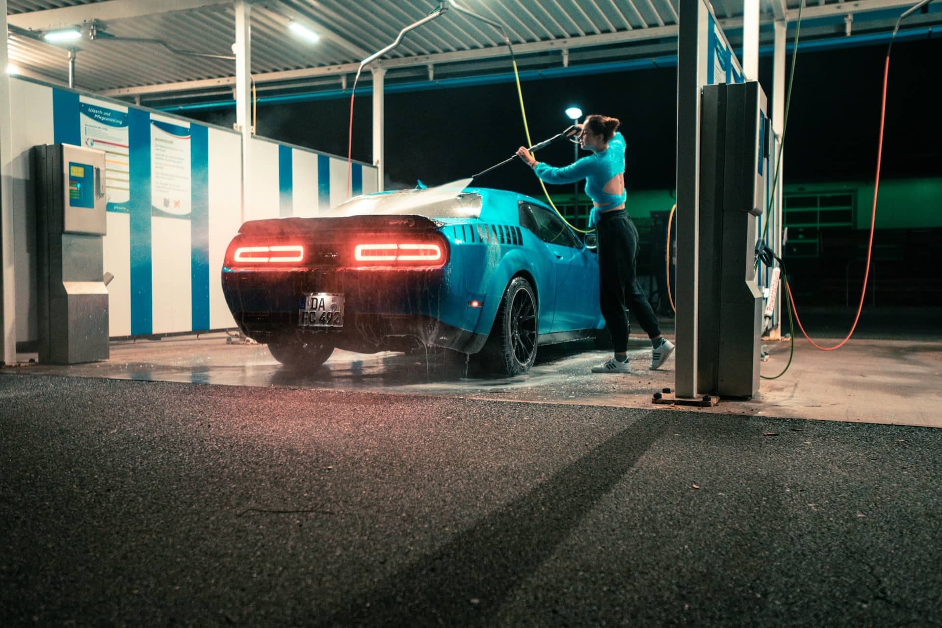 a woman washing it's blue car in a self service car wash